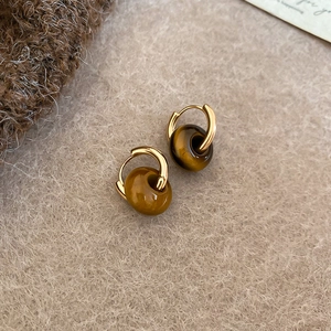 Detailed close-up of golden metal earrings with natural brown tiger eye stone beads