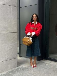 Street style shot of a woman in a red half-zip sweatshirt and denim skirt with a woven bag