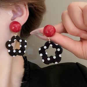 Close-up of earrings featuring red beads and black floral pendants with white polka dots