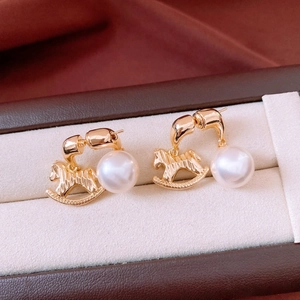 Detailed close-up of golden rocking horse earrings with elegant pearls on a velvet display