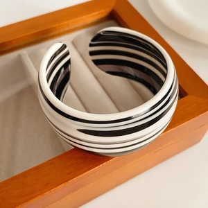 Close-up of a striped acetate open bangle on a dark wood display tray with a glossy finish
