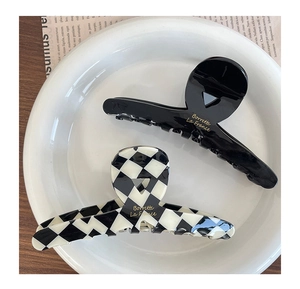 Close-up of black and checkered acetate hair claws with gold lettering in a ceramic dish