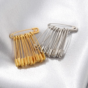 Detailed shot of 18K gold and silver plated metal safety pins on silver silk fabric