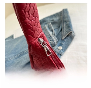 Close-up of red woven leather tote featuring a silver zipper and iconic knotted handle