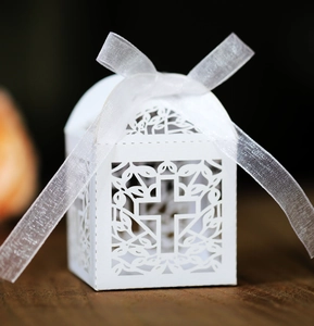 Detail showing white laser-cut hollow candy box with cross pattern and silk ribbon