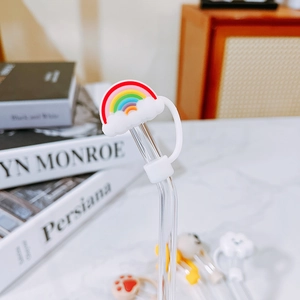 Detail of curved glass straw featuring a cute rainbow cloud dust plug on a desk