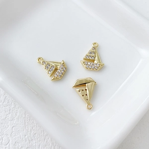 Macro detail of 14k gold plated sailboat charms with tiny zircon stones on a ceramic tray