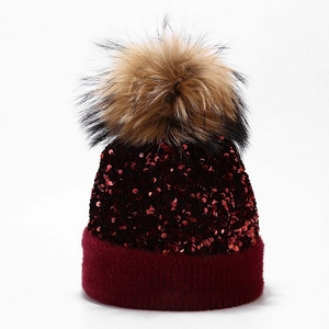 Detail of burgundy sequin knitted beanie with fluffy raccoon fur pompom and plush cuff