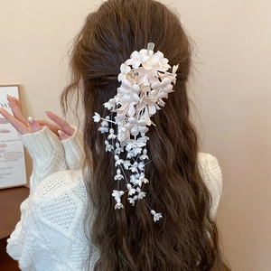 Detailed view of cream floral hair clip with long tassels and pearl beads on hair