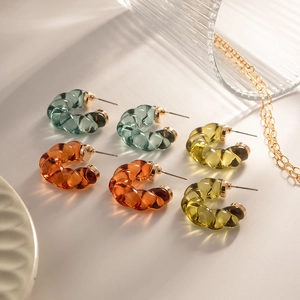 Colorful C-shaped resin hoop earrings in teal, amber, and yellow on a textured background