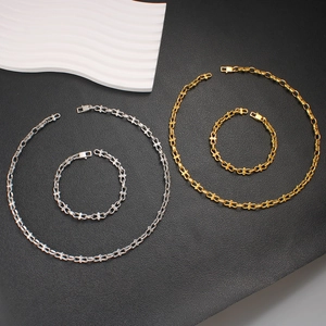 Gold and silver stainless steel chain necklace and bracelet set on black textured surface
