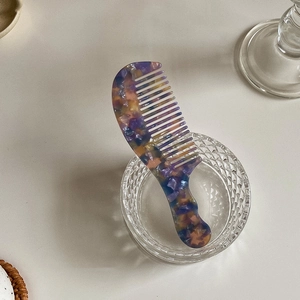 Detail of a portable tortoise shell acetate comb with purple and yellow patterns in a glass