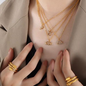 Gold zodiac sign necklaces and twisted steel cable rings worn with minimalist style