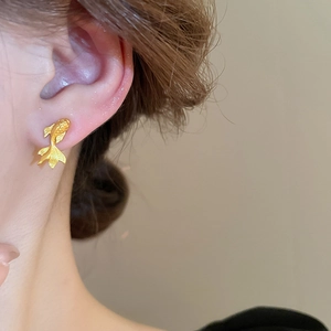 Detail of gold fish stud earring showing matte texture and intricate scale craftsmanship