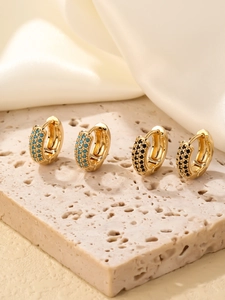 Détail de créoles rondes dorées avec pierres incrustées turquoises et noires sur pierre
