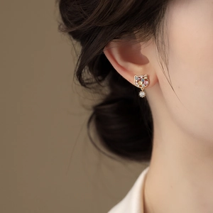 Close-up of gold plated zircon cat stud earrings worn by a model in natural light