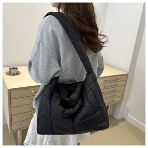 Detail of a black quilted nylon tote bag worn by a model in a minimalist lifestyle setting