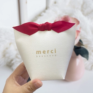 Textured white pillow gift box with red ribbon bow and gold merci beaucoup lettering