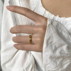 Close-up of a gold star engraved ring worn by a model holding a glass cup