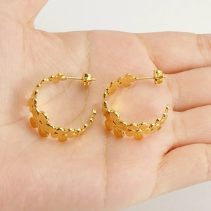 Detailed close-up of gold daisy floral hoop earrings held by hand showing the size and texture