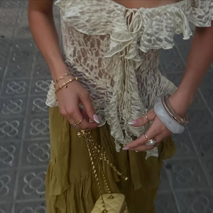 Detailed shot of an off-white lace ruffle top paired with a pleated mustard yellow skirt
