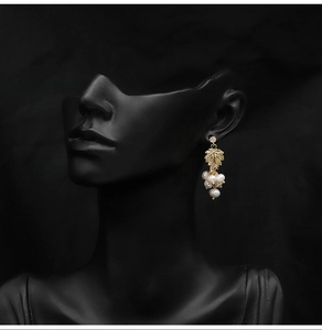 Detailed close-up of a grape-shaped pearl earring with gold leaves and rhinestone on a model