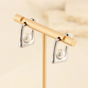 Macro detail of silver square geometric stud earrings with white pearl inlay on gold stand
