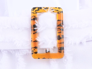Detail of amber tortoiseshell buckle on a white textured belt with fringe edges