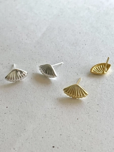 Detailed view of fan-shaped silver and gold stud earrings on a textured stone surface