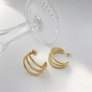 Close-up of golden triple-layered C-shaped earrings with fine textured metallic surface