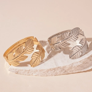 Two-piece set of gold and silver leaf-shaped open bracelets on a minimalist stone
