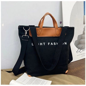 Close-up of black canvas tote bag with brown leather handles and Light Fashion lettering
