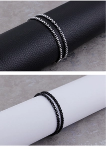 Close-up of square pearl box chains in silver and black finishes on textured pedestals