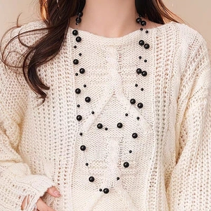 Macro view of long layered black bead necklace styled on a white cable knit sweater