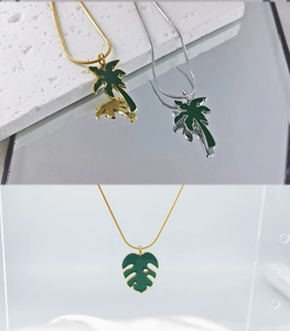 Détail de colliers en or 18 carats et argent avec pendentifs palmier et monstera en émail vert