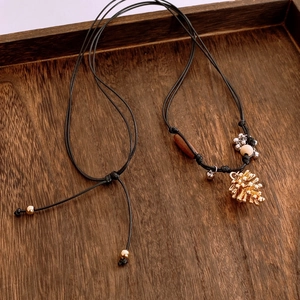 Détail du pendentif pomme de pin en métal avec perle en bois sur cordon noir réglable