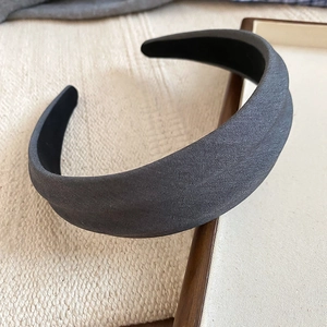 Detail eines dunkelgrauen breiten Stoff-Haarreifens auf einem Holztablett im Minimal-Stil
