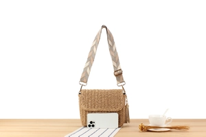 Macro detail of hand-woven straw crossbody bag with geometric strap and tassel on wood