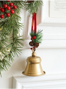 Close-up of golden Christmas bell with pine cones and red berries on a white mantel
