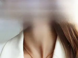 Detail of a thin gold-plated pendant necklace on a model wearing a white professional blazer