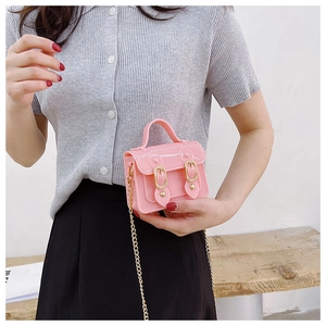 Pink mini crossbody bag held in hand showing compact size and gold chain detail