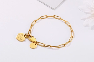 Detail of gold paperclip chain bracelet with engraved heart and round charms