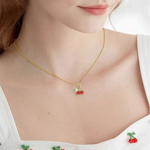 Close-up of a realistic red cherry pendant necklace on a gold chain worn by a model