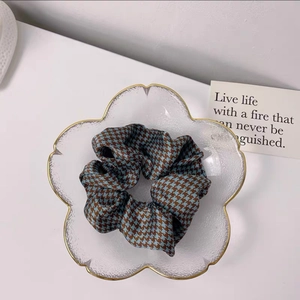 Close-up of a blue and brown houndstooth silk scrunchie in a gold-rimmed glass dish