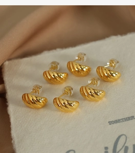 Detailed view of three pairs of gold twisted horn hoop earrings on white card display