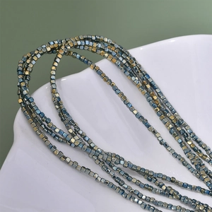 Close-up of 2mm square hematite beads in metallic blue and gold in a white shell bowl