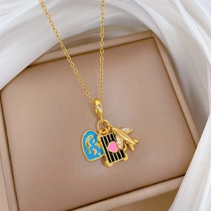 Detail of gold necklace with blue heart map, black suitcase and airplane charms on silk
