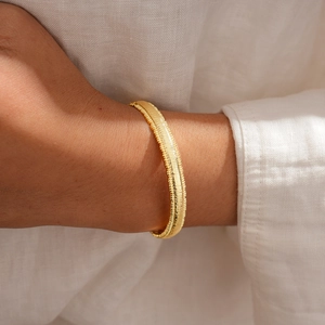 Macro shot of 18k gold plated textured metal bangle showing detailed horizontal stripe carving