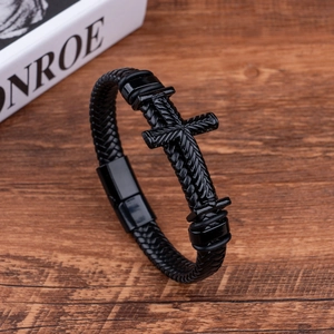 Men's black braided leather cross bracelet with magnetic clasp on dark wooden desk