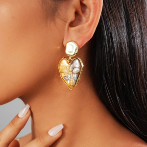 Vintage heart earrings with imitation pearls and stones worn by a model in nature
